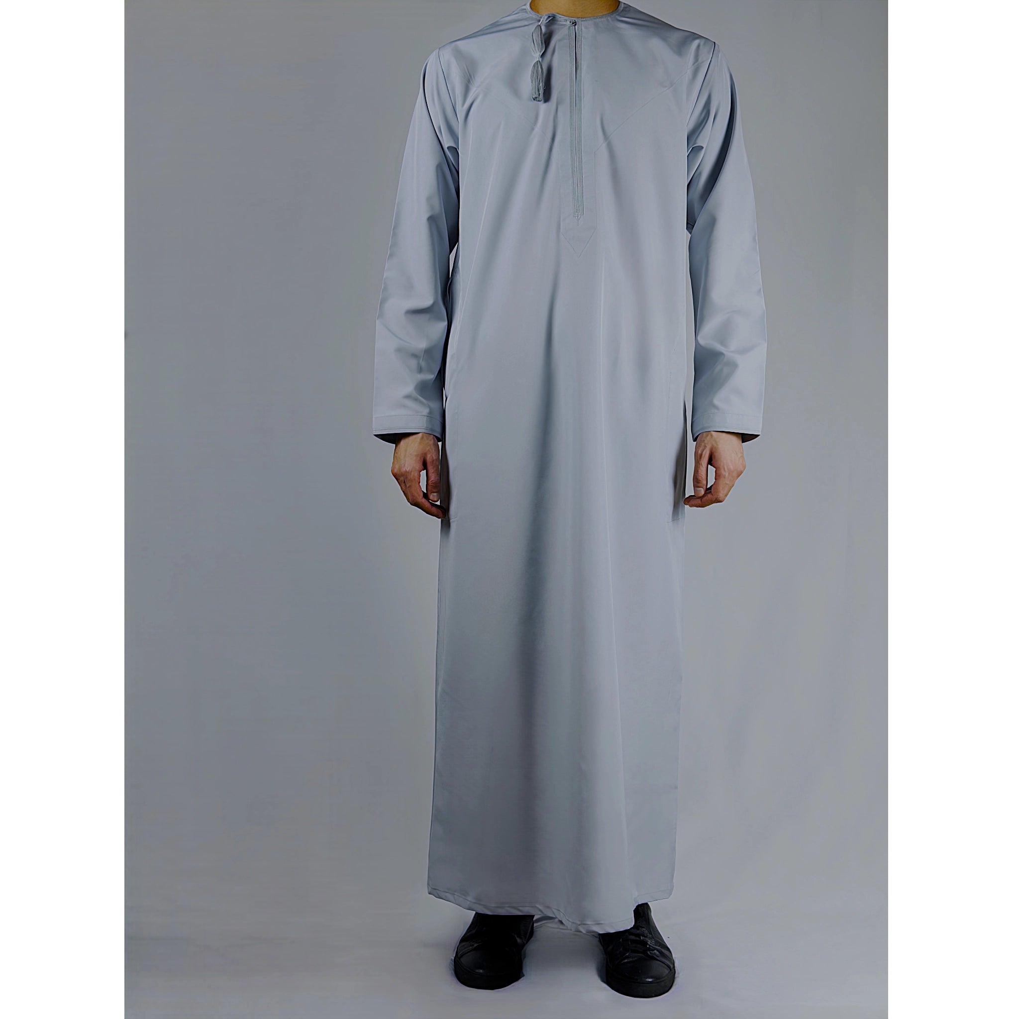 man wearing light blue Omani thobe on a against a plain background