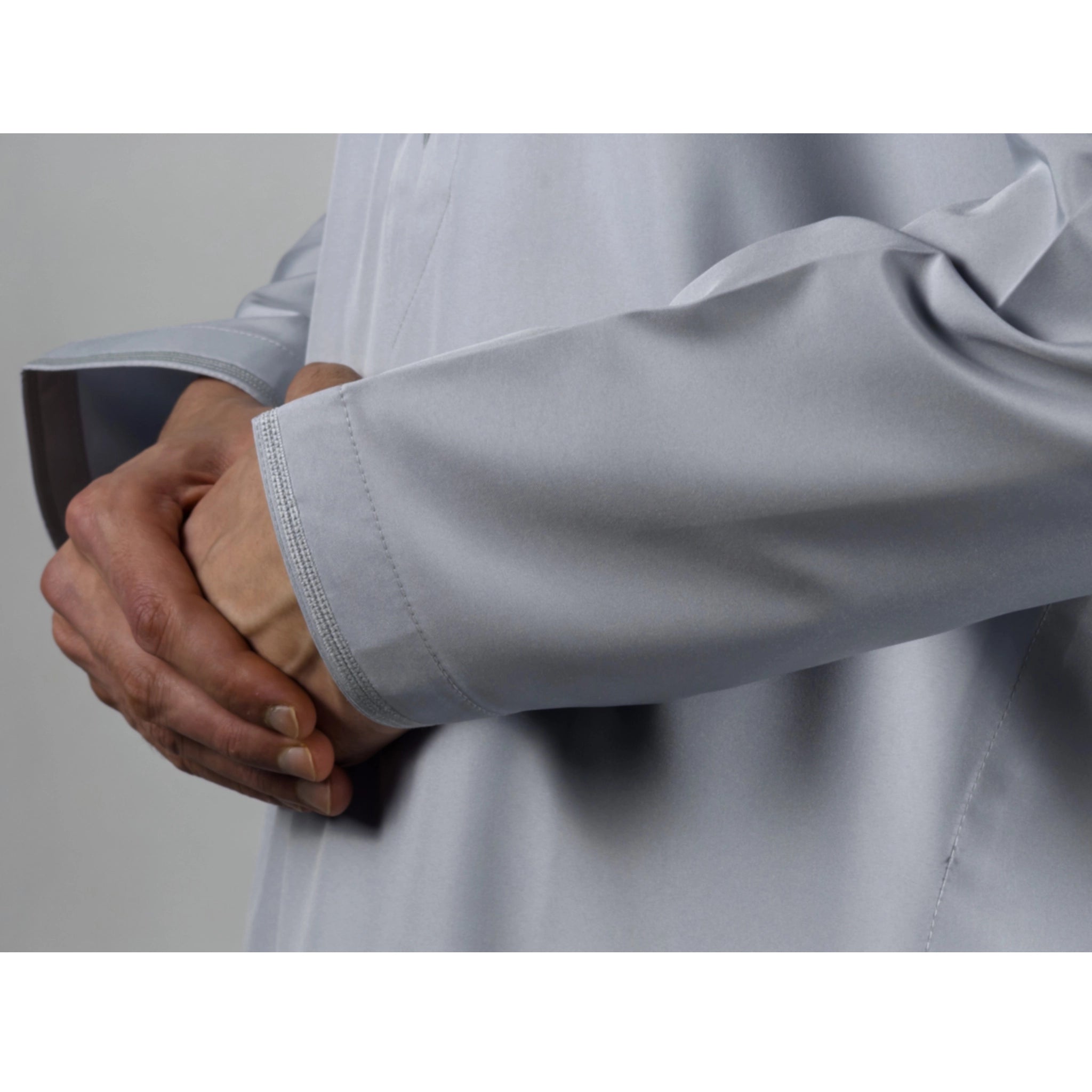 Close-up of a person wearing a light fog blue  long-sleeve Omani Thobe with hands clasped together.