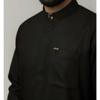 A close-up of a man wearing a midnight green long-sleeve collared shirt with a chest pocket and small gold-toned logo details, including an embroidered ND logo and a decorative button at the collar.