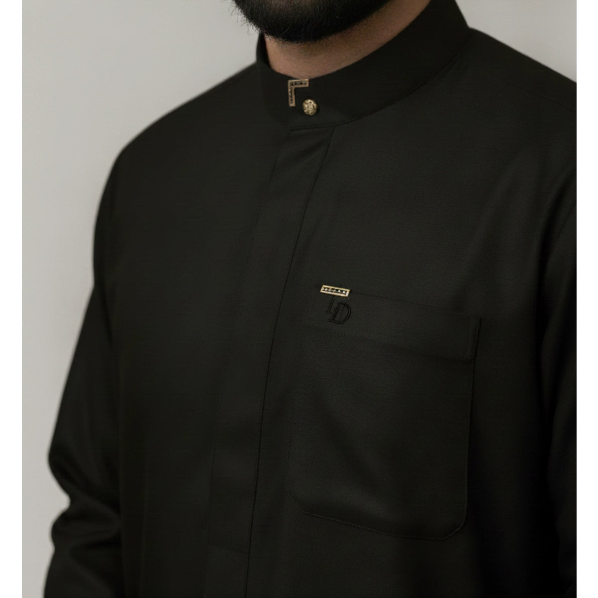 A close-up of a man wearing a midnight green long-sleeve collared shirt with a chest pocket and small gold-toned logo details, including an embroidered ND logo and a decorative button at the collar.