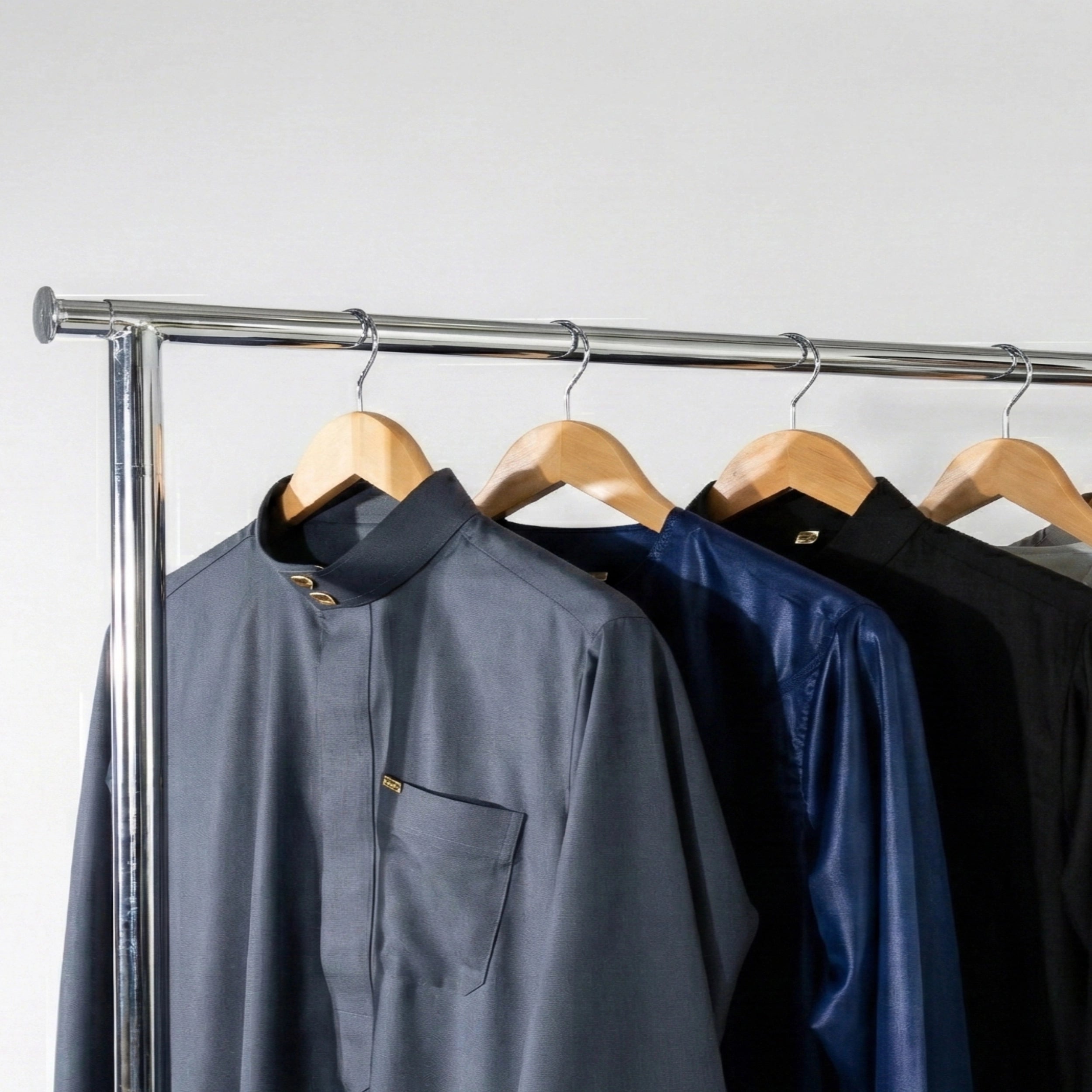 Islamic thobes in grey, blue, and black hanging on a rack against a white background